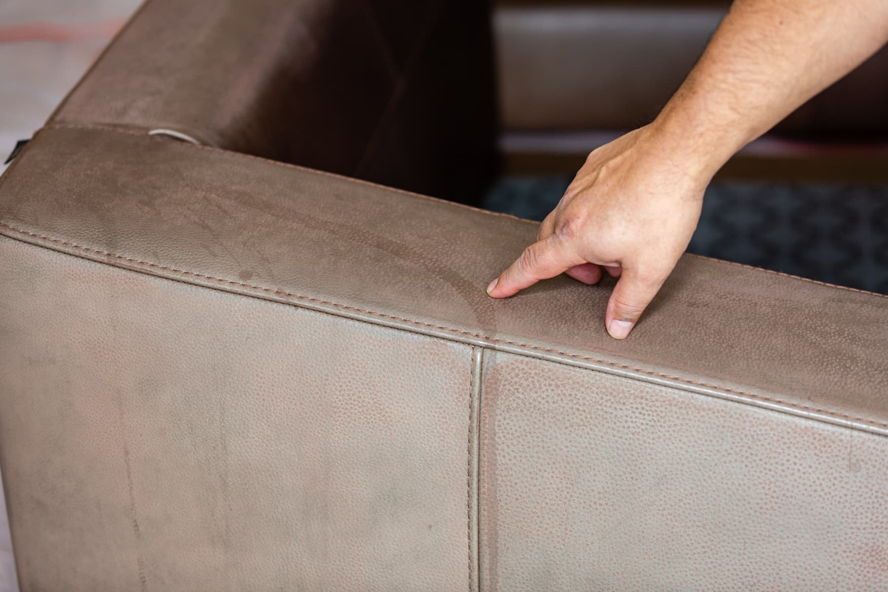 A hand points to faded areas on a brown leather chair arm