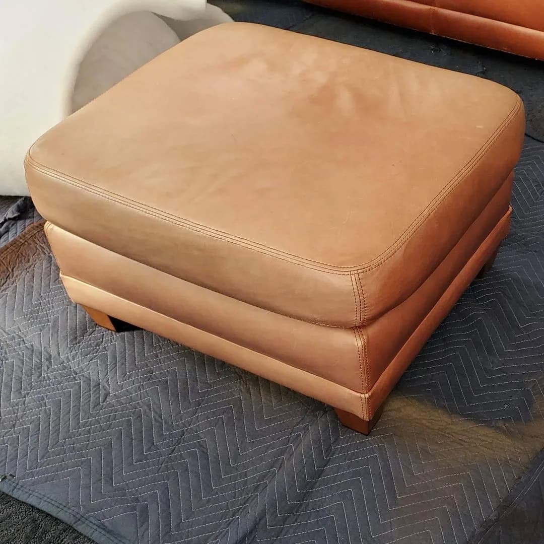 Tan leather ottoman on a protective moving blanket